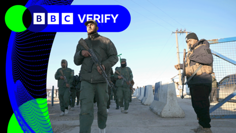 Men armed with AK-47-style rifles and wearing green military clothing walking inside a camp