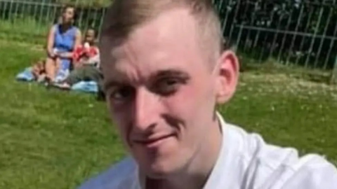 Robert Fisher, with short, fair hair and a white shirt, is pictured in a park.