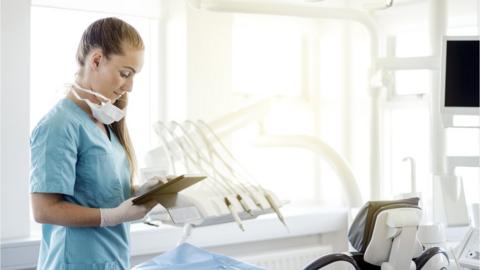 A dentist looks at an ipad next to the dentist chair