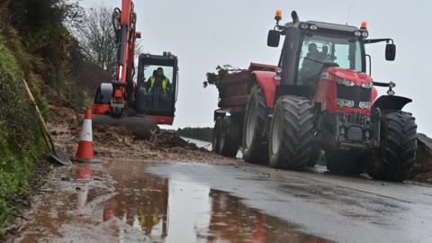 A digger and a tractor work to clear a landslip on the Coast Road