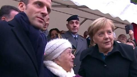 President Macron next to Paulette Monier (C) and Chancellor Merkel