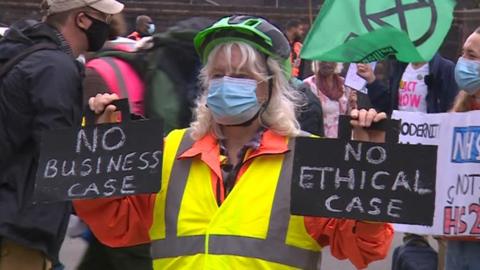 A woman holds signs reading "no business case" and "no ethical case"