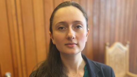 Woman - council leader Heather Woodbridge - looking at camera, with dark hair tied back, wearing a green top and a dark jacket