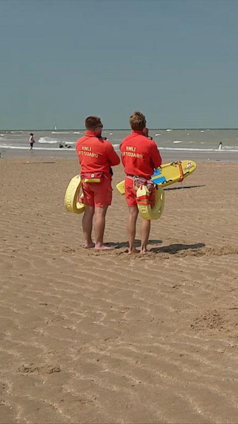 Two lifeguards on a sandy beach holding boards