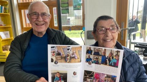 An elderly couple holding up a personalised newspaper