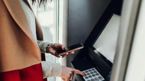 Woman getting cash out while holding her phone at a ATM