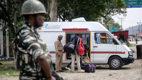 An Indian security forces personnel stands guard as Kashmir police men check luggage