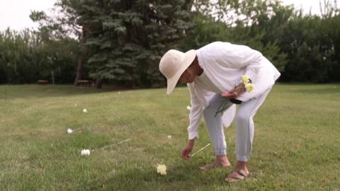 Edna Elias places flower on unmarked grave