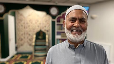 Nurul Chowdhury stands wearing traditional Muslim dress, inside Ipswich Mosque.