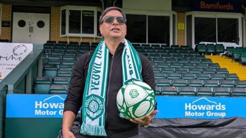 Prabhu Srinivasan wearing a Yeovil Town scarf and holding a football at Huish Park