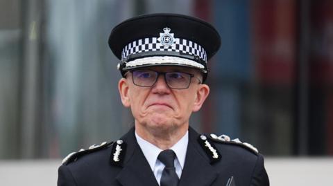Sir Mark Rowley pictured outdoors, wearing his full uniform and glasses. His expression is serious, with the edges of his mouth turned down.
