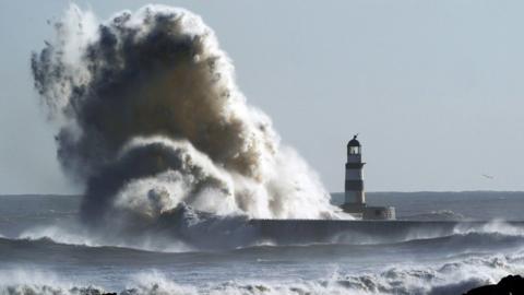 Big wave breaks next to lighthouse