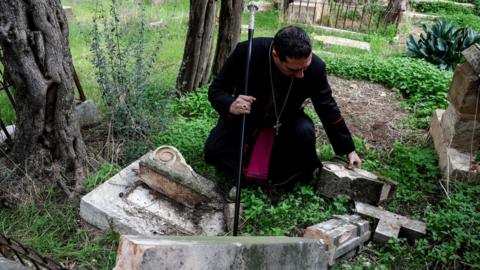 Archbishop Hosam Naoum inspects a desecrated grave at the Protestant Cemetary on Mount Zion in Jerusalem (4 January 2023)