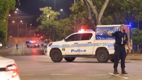 A police car and officer block off a major road in Darwin where the alleged gunman was arrested