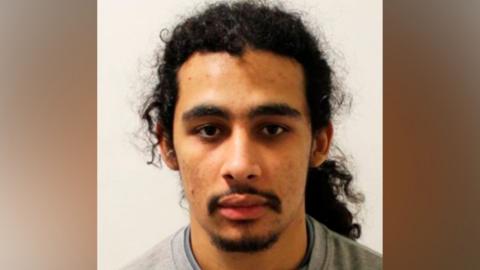 A close-up mugshot of Aderahman Boumzough wearing a grey crew-neck jumper over a dark undershirt, positioned against a plain white background.