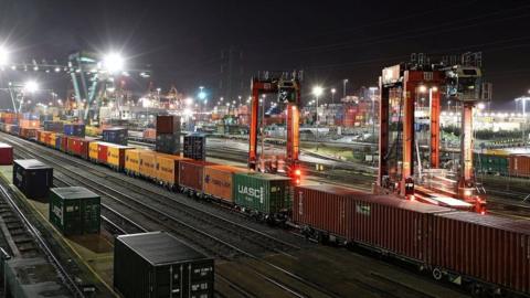 Rail tracks with containers on freight trains at night with dozens of flood lights