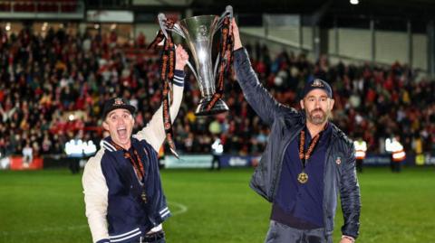 Rob McElhenney and Ryan Reynolds lift a trophy