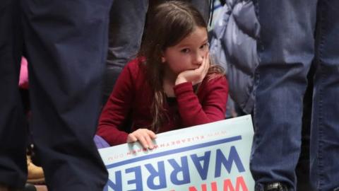 Young girl sits with Elizabeth Warren campaign sign at a New Hampshire rally, February 2020