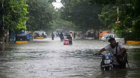 Commuters push their two wheelers through a flooded street after heavy rain shower in Chennai on November 7