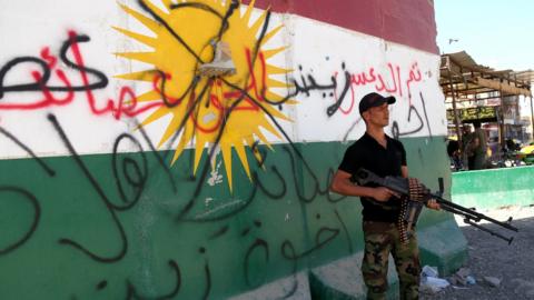 A Shia militiaman stands next to a crossed-out Kurdish flag in Tuz, south of Kirkuk city, Iraq (17 October 2017)