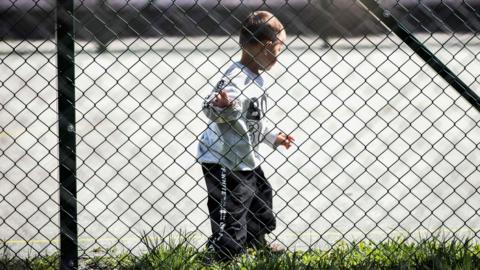Image shows a young Kosovar child returned from Syria walking in the compound of a foreign detention centre