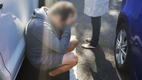 A suspect in custody kneels down and holds his head