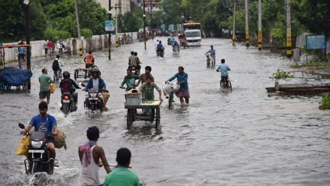 Commuters make their way on a waterlogged road following heavy monsoon rain in Patna