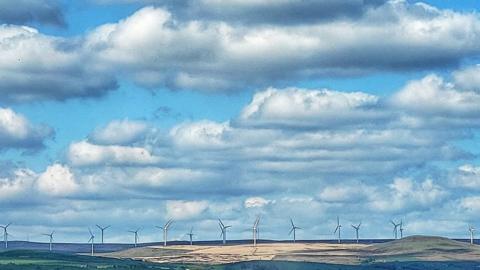 Blue sky with layer of white cloud sit over a wind farm which stretches across a number of fields