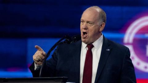 Tom Homan, wearing a suit, talks into a microphone.