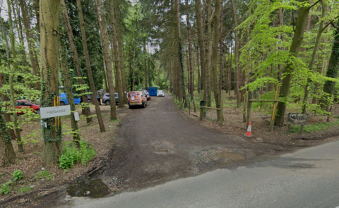 Hallswood sign beside a muddy track trailing out of sight, between trees, with a parked van and several cars visible 