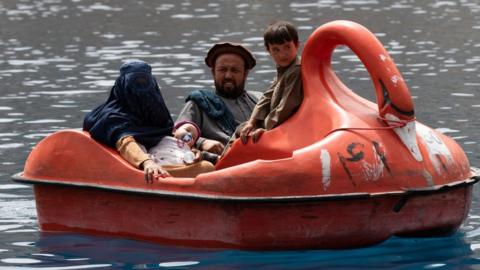 A man and a woman ride with children on a boat in the Band-e-Amir national park