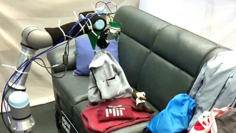 A robot picks up an item of clothing to look for a missing remote control