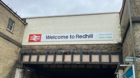 A grimy brick façade with a sign saying 'welcome to Redhill'