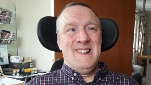 Headshot of Mark Williams smiling at the camera in a wheelchair