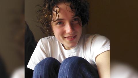 Evangeline Wilson, with curly hair, wearing a white t-shirt and blue trousers.