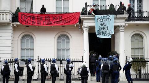 Police officers in riot gear force entry to the property in Belgrave Square