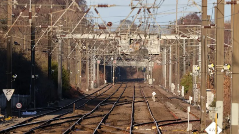 A section of track in Devizes with electrical wiring, stanchions and other railway infrastructure visible.