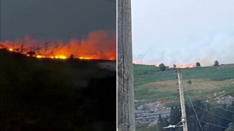There are two images combined, on the left hand side is an image of a wildfire burning on a grassy mountain at night. The image on the right is the same mountain burning during the day time, there is also a large telephone pole in the foreground of the left image.