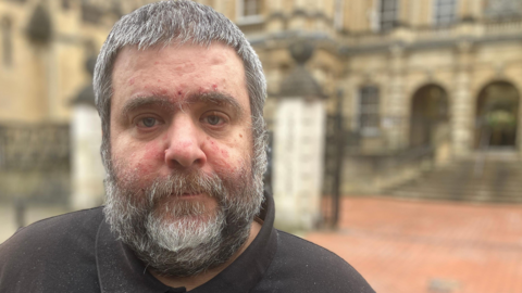 Barry O'Sullivan, who has grey, short hair and a grey, short beard, stood in front of Reading Crown Court. He is wearing a black T-shirt.