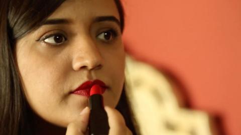 A young Pakistani woman puts on red lipstick