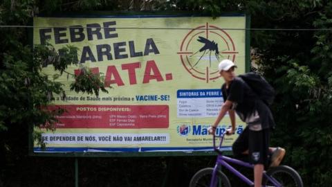 A young man passes by a billboard inviting people to vaccinate against yellow fever, at Mairipora municipality, in Sao Paulo, Brazil, 19 January 2018