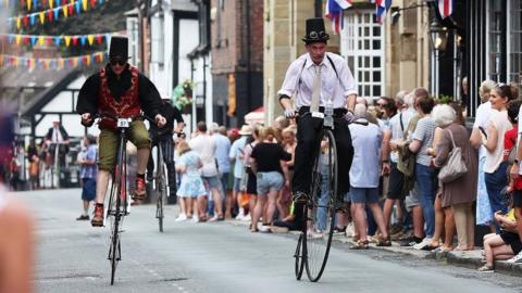 two men in fancy dress ride through market street in front of crowds