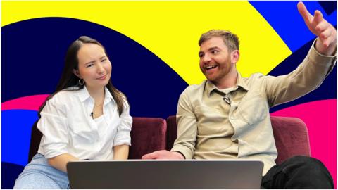 A confused looking woman and a smiling man, sat on a sofa with a laptop