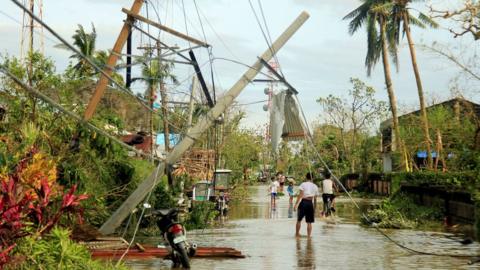 Residents walk past partially toppled electric posts after Typhoon Nock Ten hit Malinao, Albay in central Philippines