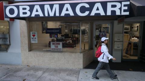 A pedestrian walks past the Leading Insurance Agency, which offers plans under the Affordable Care Act, in Miami