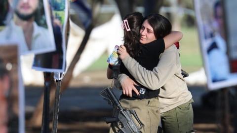 Israeli soldiers hug as they look at pictures of the Nova music festival victims at the site of the festival near Kibbutz Reim