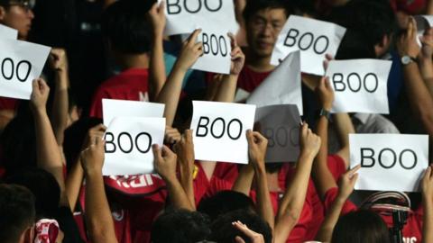 People turn their back and boo while holding up placards during the Chinese anthem at the start of the Qatar 2022 World Cup qualifying football match between Iran and Hong Kong
