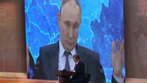 Dmitry Peskov in front of a screen showing President Putin