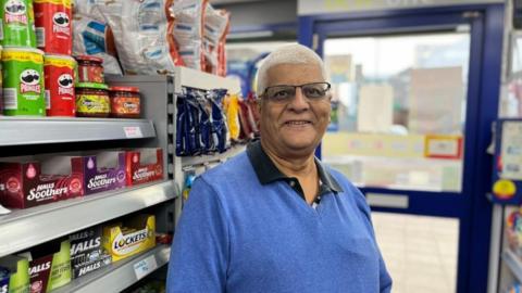 Man with short white hair and glasses in a small local shop