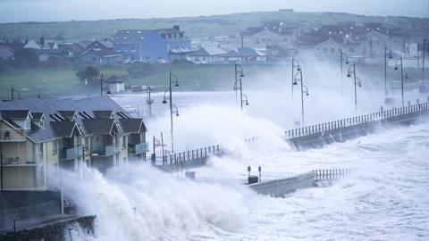 Waves lash the Irish coast, spraying buildings and a road